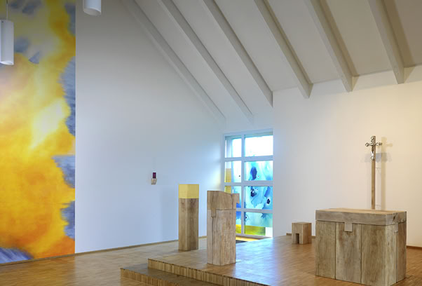 Pfarrer-Franz-Böhm-Haus, Kapelle St. Ursula, Monheim. Wandgestaltung: Seccomalerei mit mineralischen Pigmenten auf Putz.  Fenstergestaltung: Dreischichtige Glasintarsie, Zuschnitt aus Opal- und Echt-Antiküberfanggläsern, mehrfach geätzt, flächig auf Sicherheitsglas laminiert und als zusätzliche innere Scheibe montiert.  Prinzipalien: Platanenholz, massiv, mit der Kettensäge aus dem vollen Stamm geschnitten, teilweise in Kombination mit Elementen aus glasperlengestrahltem Edelstahl.